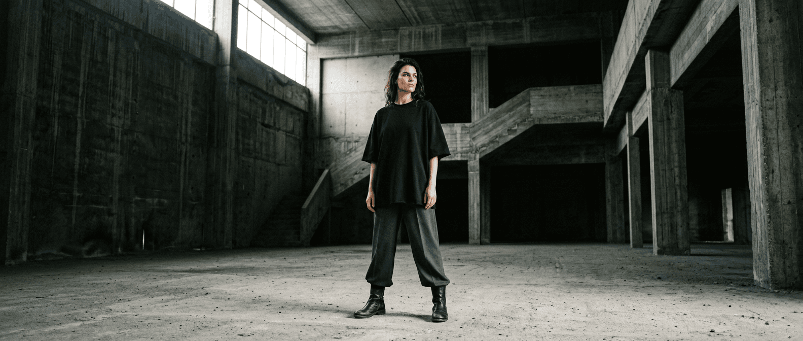 Model in an oversized black heavyweight tee standing in an empty concrete warehouse